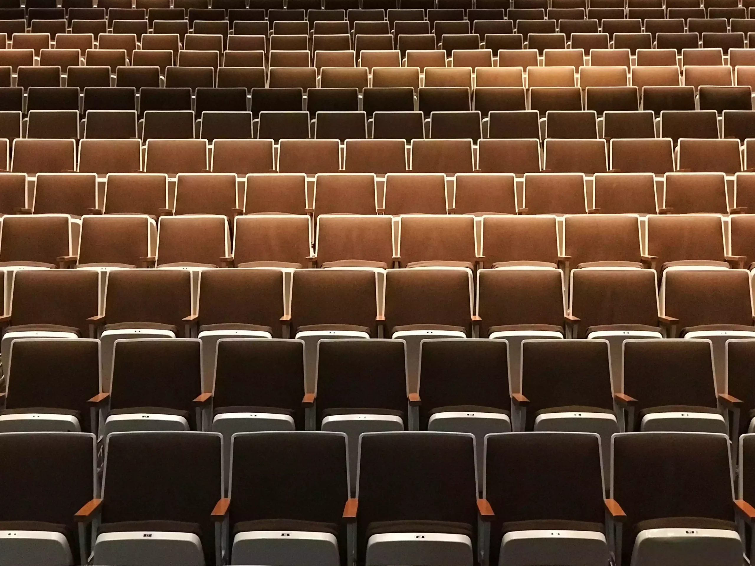 An empty auditorium with rows of brown and beige seats arranged in a symmetrical pattern, viewed from the front.